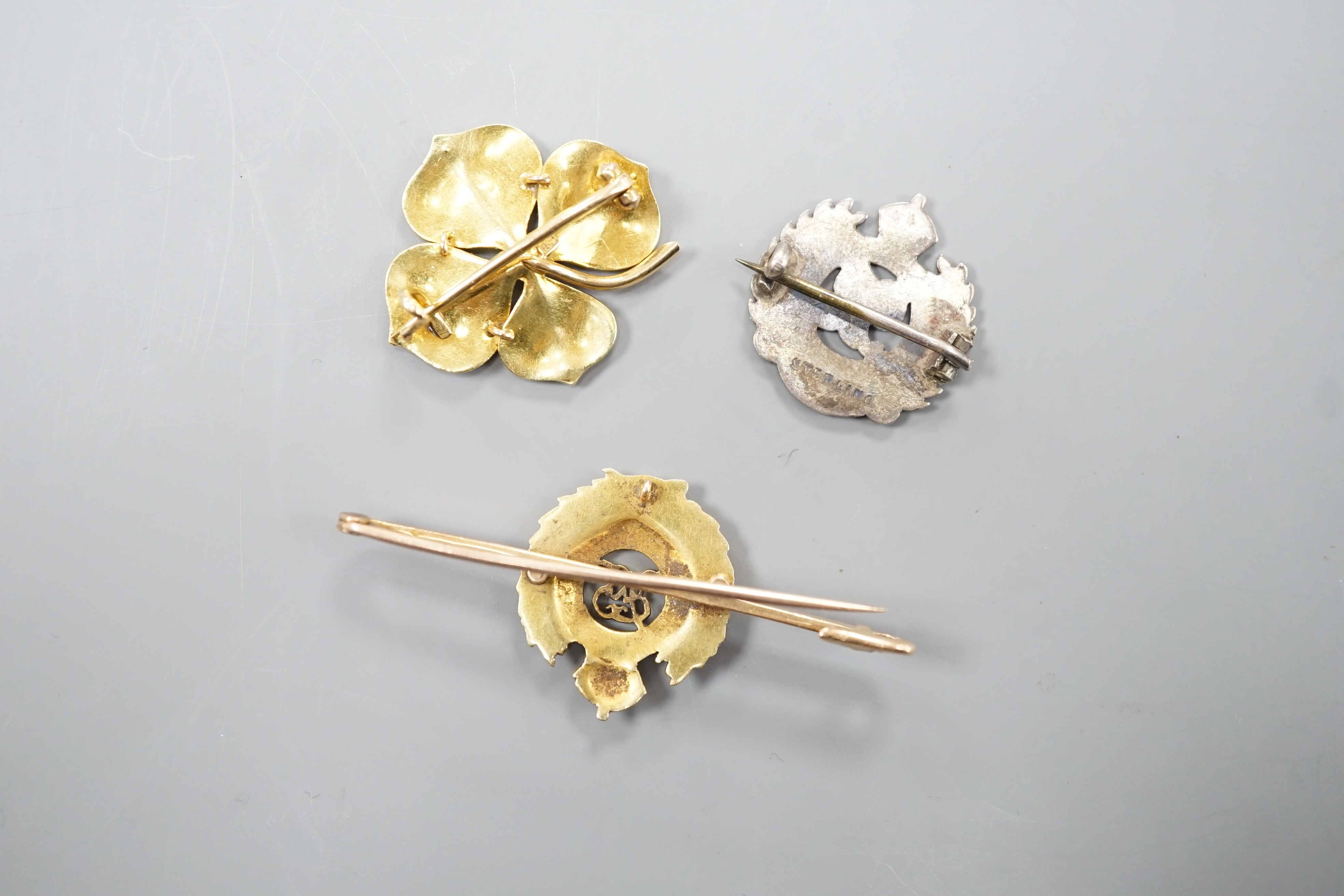 An early 20th century and two colour enamel set Royal Engineers sweetheart brooch, 5cm, gross 5.6 grams, an 18ct, seed pearl and green enamel clover brooch, 26mm, gross 6.2 grams and a sterling and yellow metal brooch.